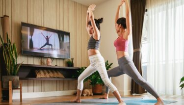 Asian woman and Little girl practicing yoga from yoga online course via smart TV at home