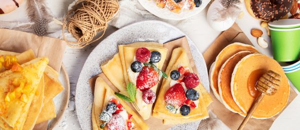 Variety of breakfast foods on a table, including pancakes, waffles and eggs.