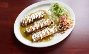 a white plate topped with two enchiladas next to a salad