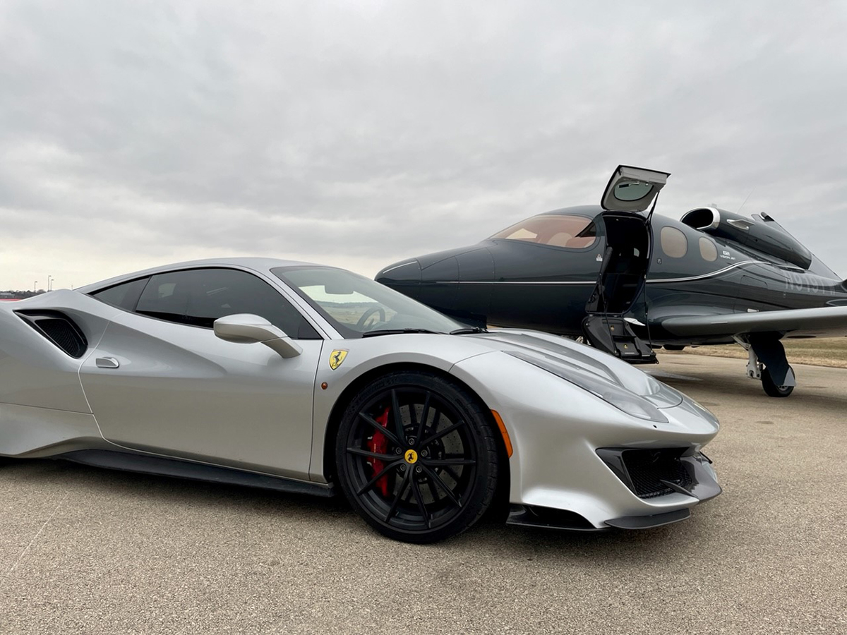 A silver Ferrari sports car parked next to a plane.