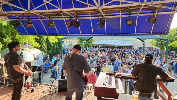 Band performs on stage to an outdoor audience on a sunny day.