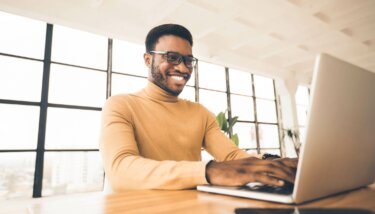 Membership founder and manager sitting at his desk and smiling while browsing membership management software on his laptop.