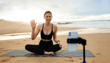 Online training. Sporty woman yoga coach recording video online training, sitting on fitness mat on