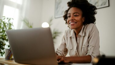 Woman sitting at desk working on laptop, smiling.